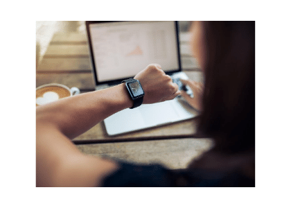 woman sitting at a desk with her laptop and coffee and checking her smartwatch for the time